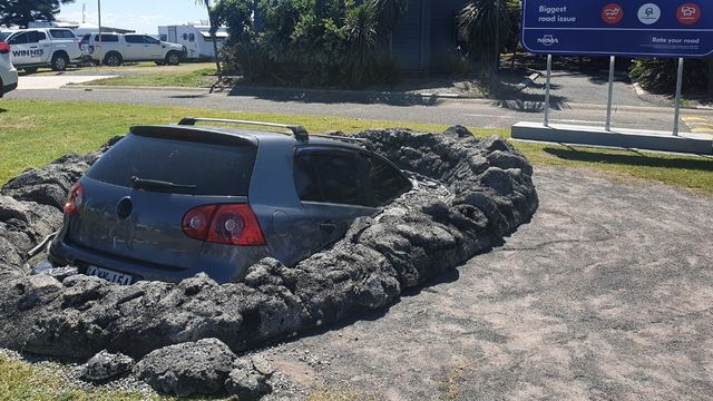 grey vehicle stuck in a giant pothole in concreted area