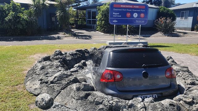 grey vehicle stuck in a giant pothole in grassy area