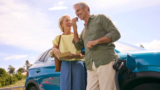 A couple eating food standing next to a charging EV