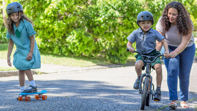Children play on scooters and bikes on an Australian street with Mum