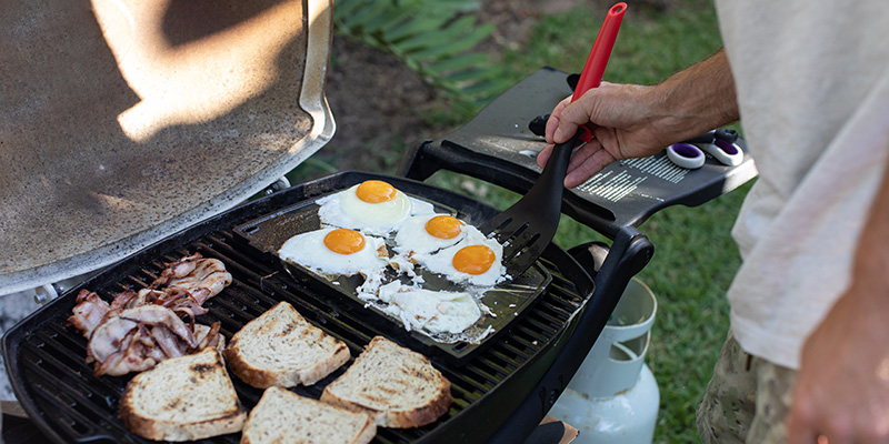 Person cooking eggs and bacon on a small camp bbq