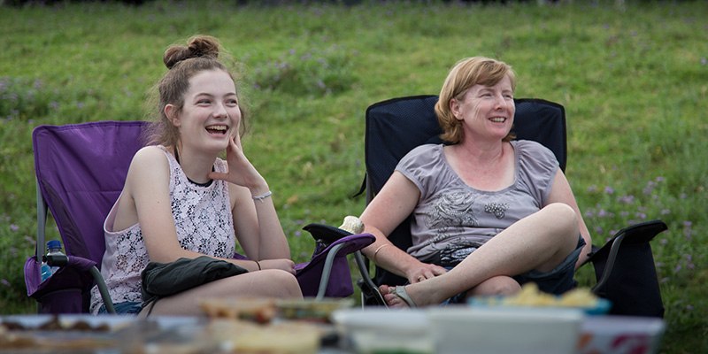 Two women, each sitting in a camp chair and laughing 