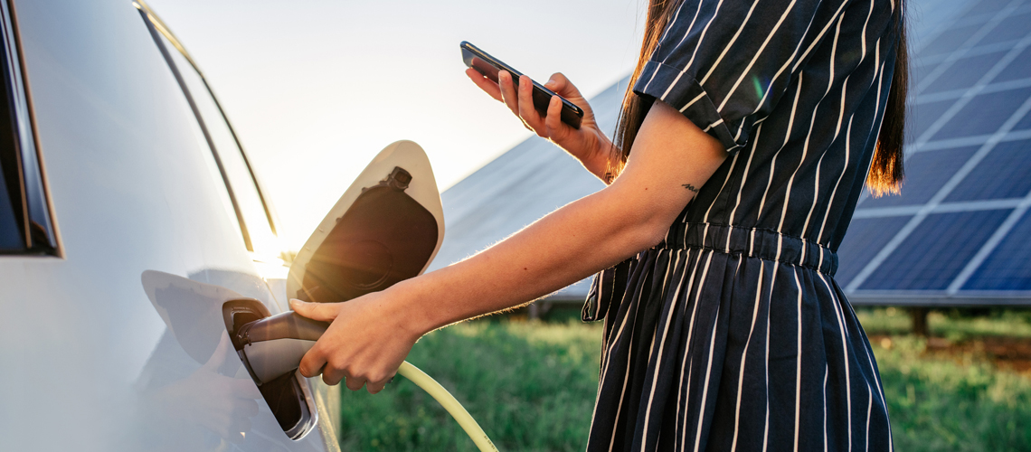 Lady charging electric car in front of solar panel