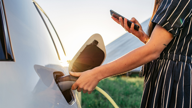 Lady charging EV in front of solar panel