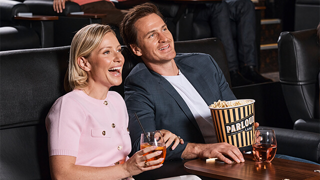 A man and woman enjoy popcorn and drinks while sitting together in a movie theater.