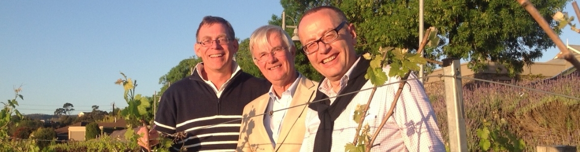 3 older gentlemen smiling in a vineyard