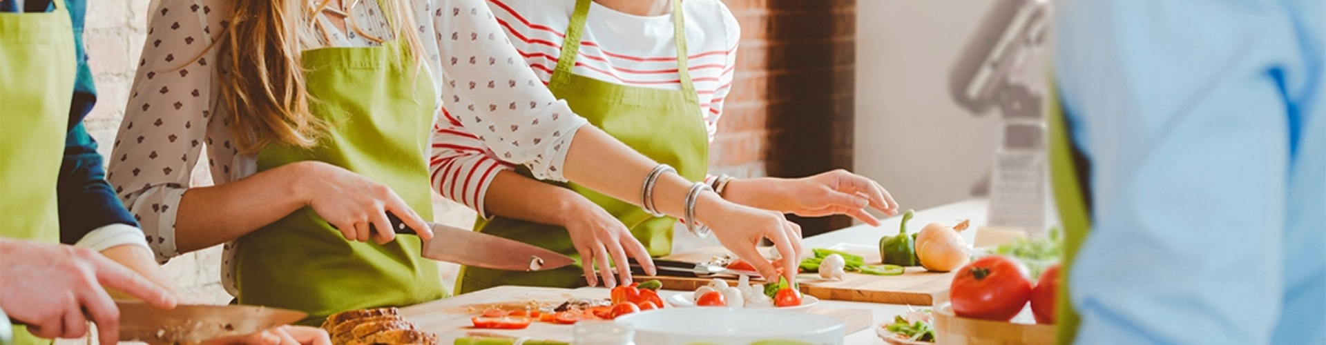 A group of people smiling, while cutting up vegetables at a countertop.