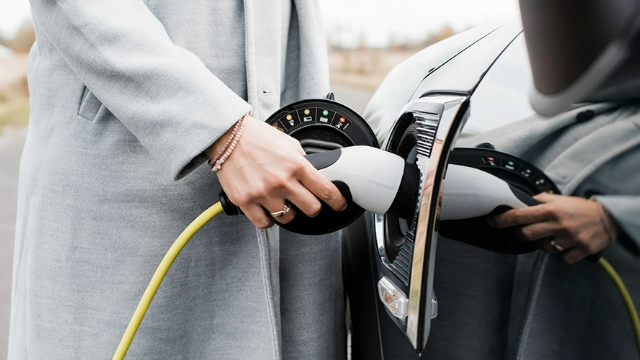 A lady wearing a grey coat, charging her electric vehicle.