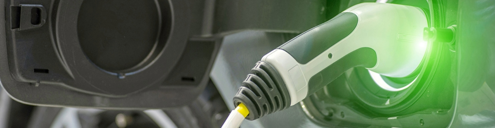 An electric vehicle charging cable plugged into a car and emitting a green light, symbolising electricity.