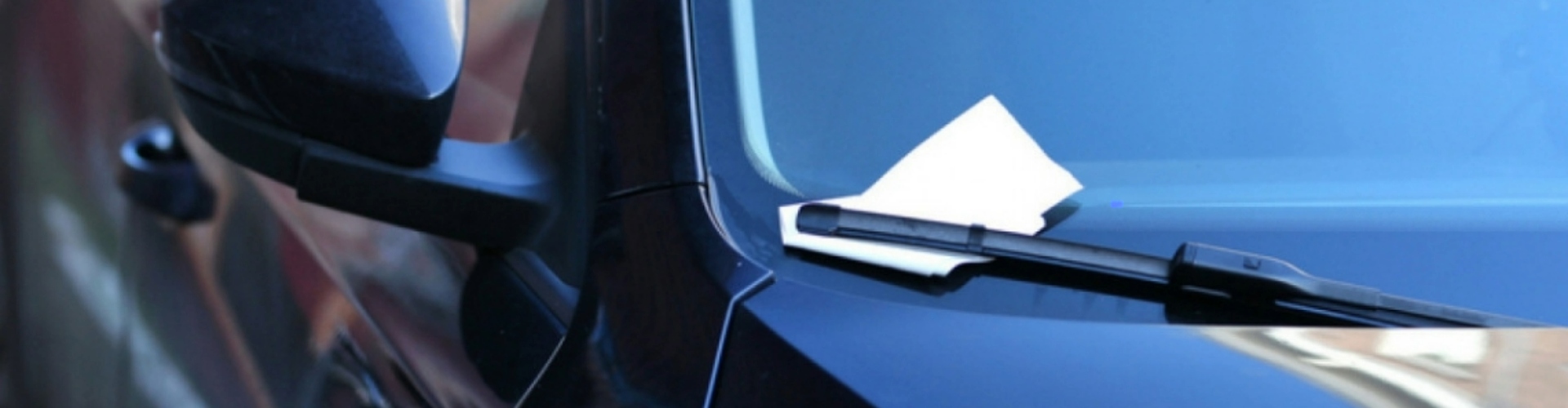 Front view of a car windshield with a parking infringement notice under the wiper.