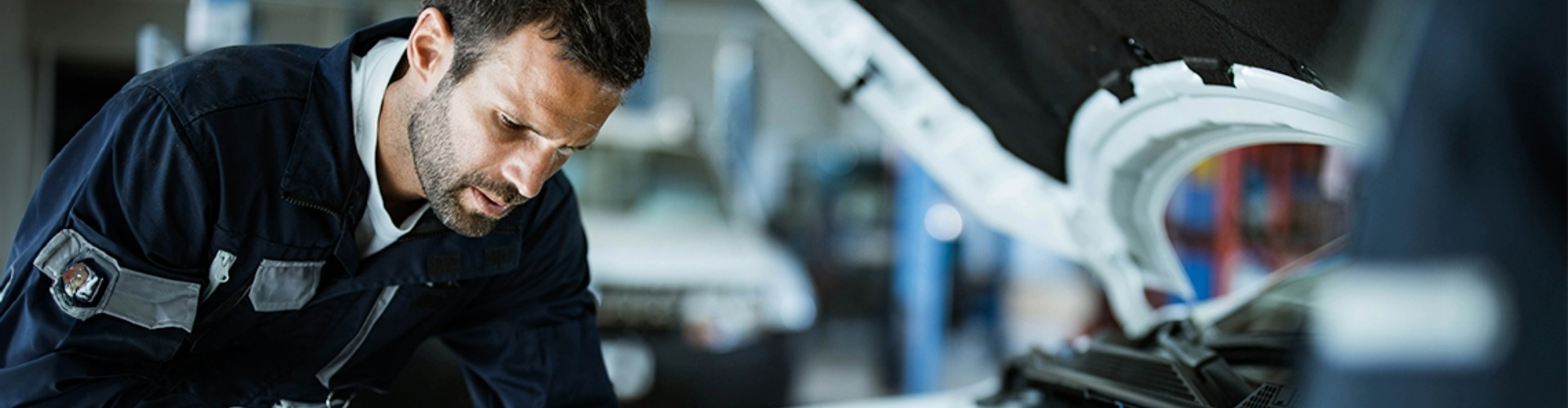 A man leaning over a car engine, testing the car battery.