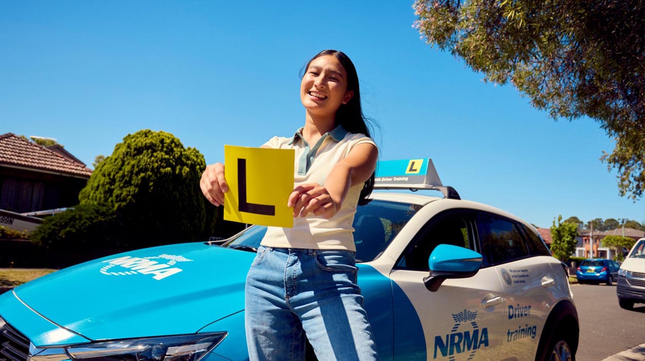 A Learner student holding L Plates in front of an NRMA car.