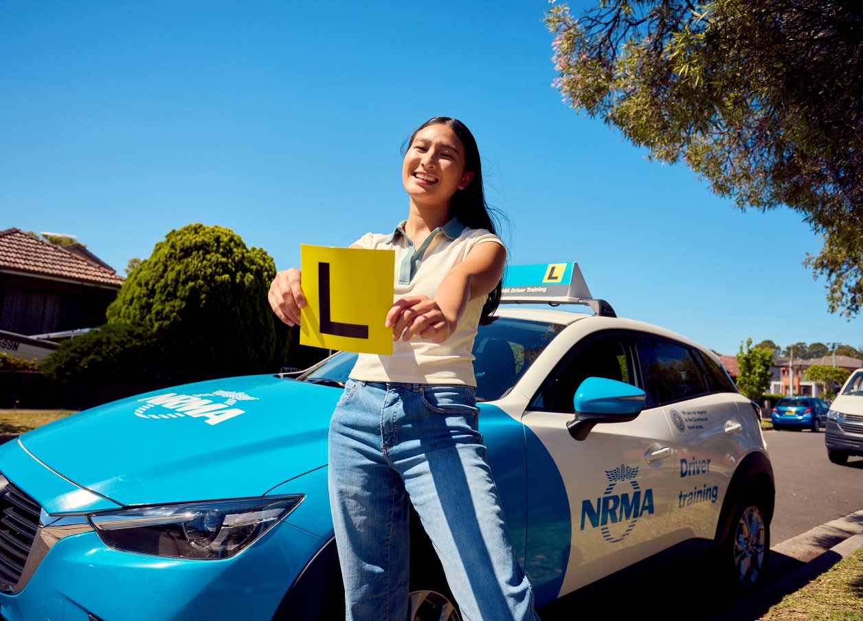 A Learner student holding L Plates in front of an NRMA car.