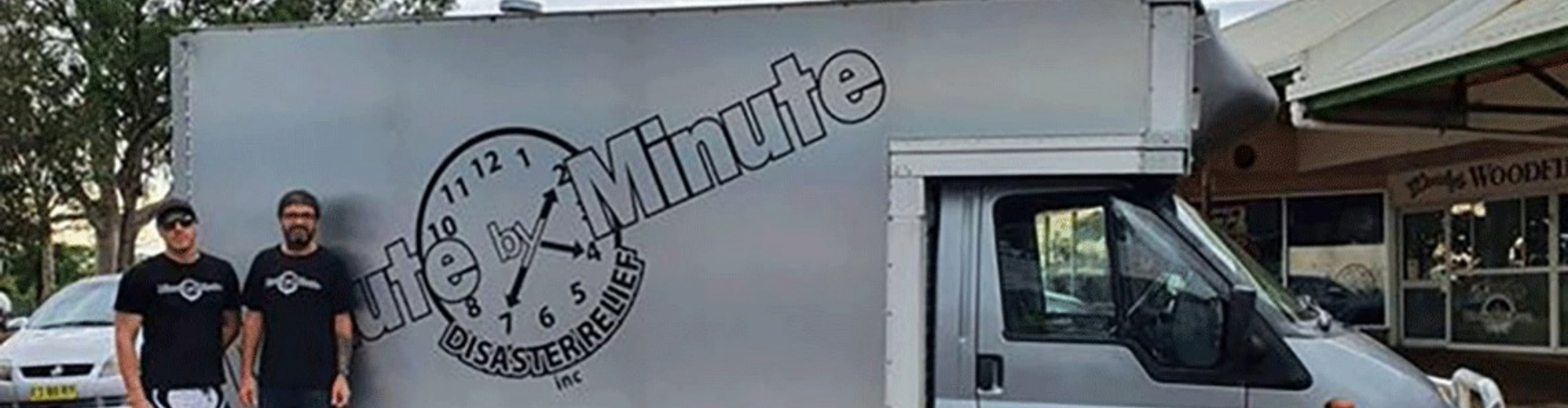 local-hero-rodney-mitchell-1920x500 Two men next to a silver moving truck with the words Minute by Minute Disaster Relief in a clock logo on its side.
