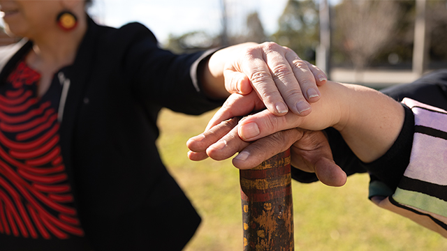 Hands stacked on a wooden stick with Aboriginal markings