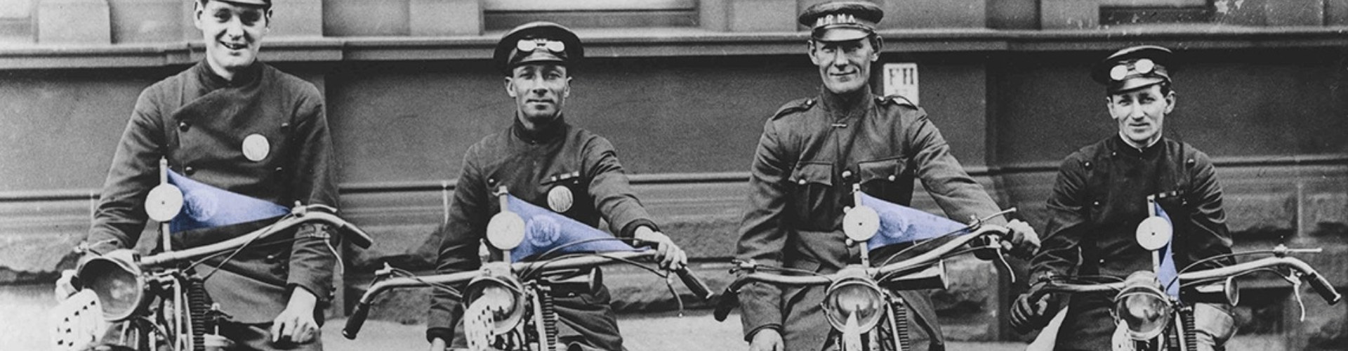 NRMA first patrols motorbikes black and white photo from the early 1920s showing a row of four young NRMA patrolmen on their motorbikes that have blue triangular NRMA flags on the handlebars