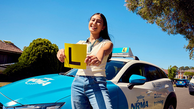A Learner Student holding L plates in front of an NRMA car