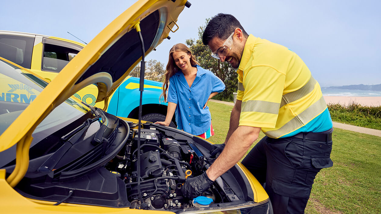 Roadside assistance staff member fixing the customer's yellow vehicle while the customer is looking on