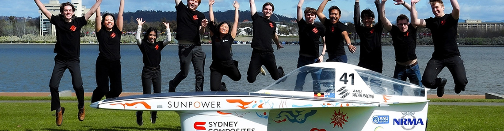 The Australian National University solar racing team leap in the air behind the vehicle they've designed