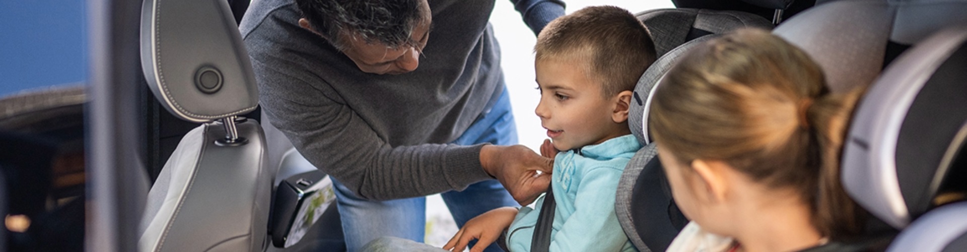male child being secured in their car seat by their dad while their sister watches