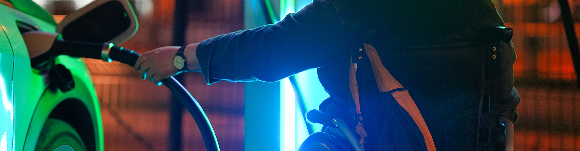 A woman using a wheelchair connects her electric car to a charging station at night