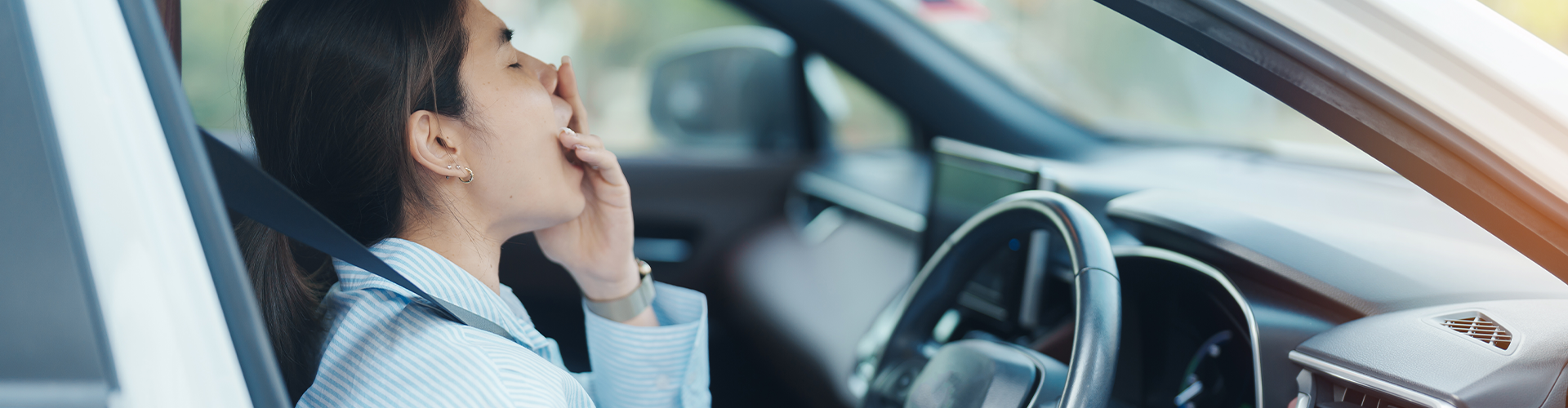 A woman yawning in the driver seat of a car
