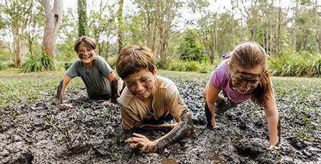 Children crawlig through mud - Bear Grylls Survival Academy