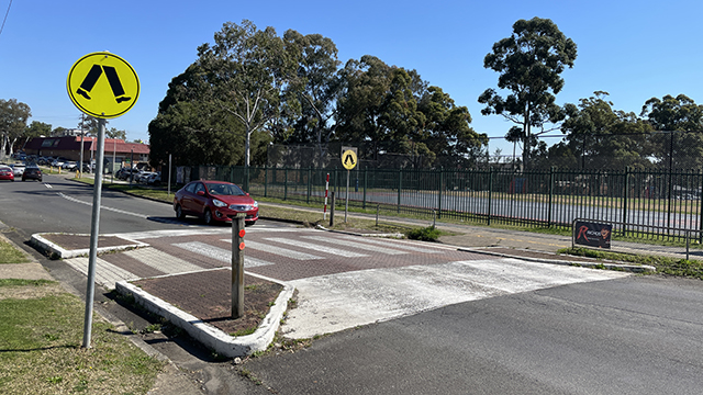 A red car driving near a pedestrian crossing