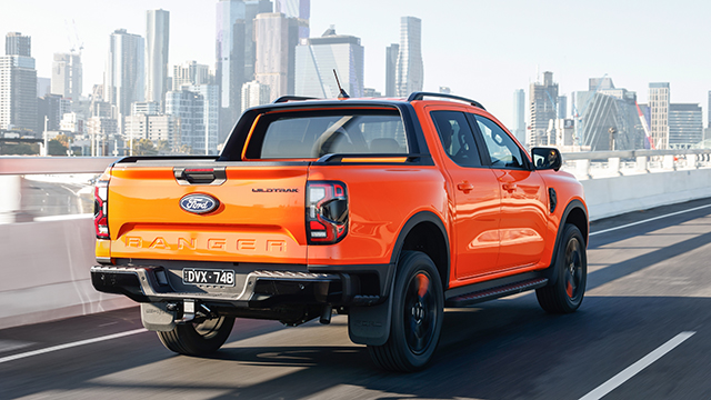 An orange ute driving near a city