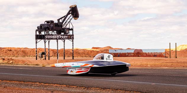 ANU Solar Racing Team solar car in front of Coober Pedy sign at solar car race event.