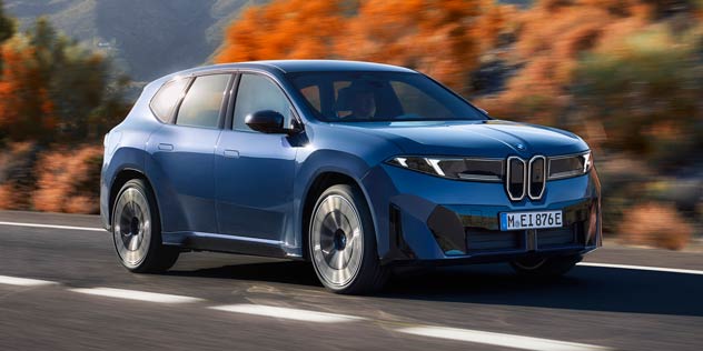 Blue BMW iX3 driving on range in front of autumn trees