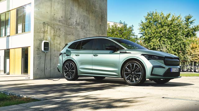 A silver green Skoda EV charges on the side of an apartment building