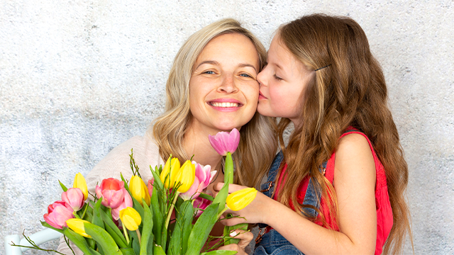 A child kissing her mother on the cheek with a bunch of flowers in the foreground