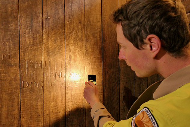 A man shining a torch on prisoner's inscription
