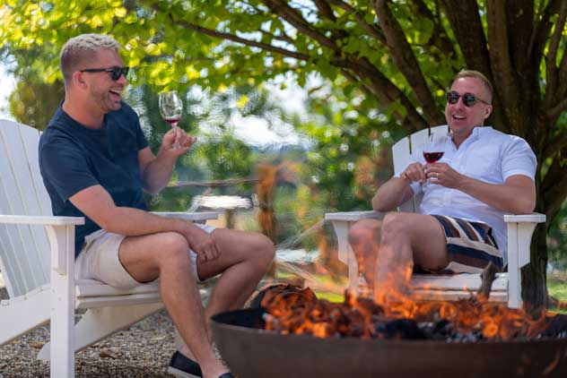 Two men sit around a fire outside enjoying a wine.