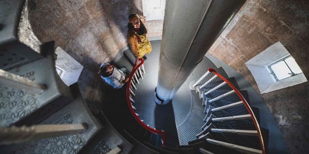 A couple wind their way up inside a lighthouse staircase seen from above