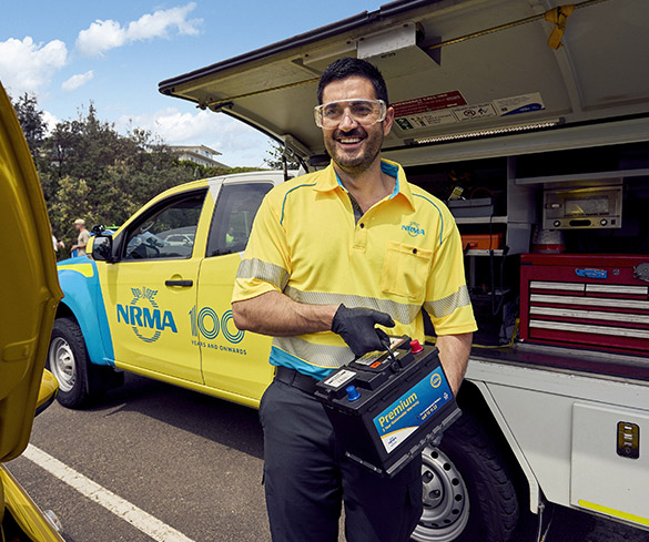 An RSA NRMA staff member in uniform smiling while holding a large battery in his hands, showcasing its size and importance.