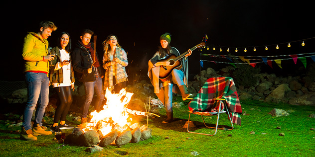 a group around a bonfire singing and playing guitar