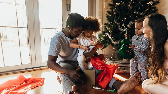 family with young children opening gifts next to a christmas tree