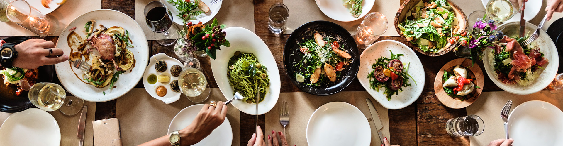 overhead shot of hands surrounding dinner plates with food on a table