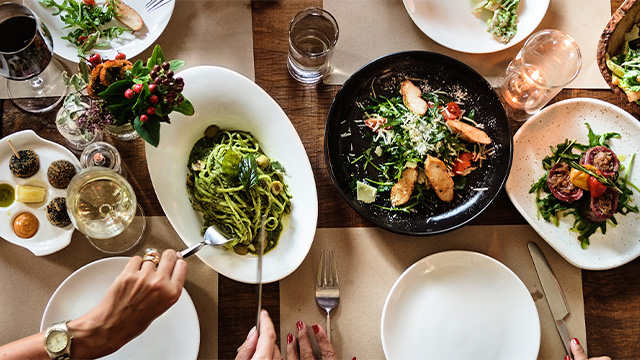overhead shot of hands surrounding dinner plates with food on a table
