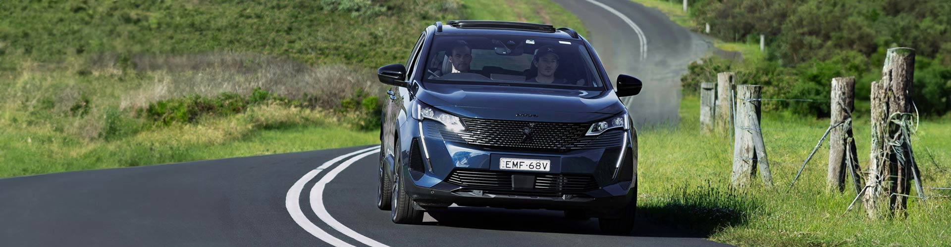 Two young men driving on a country road in a blue car