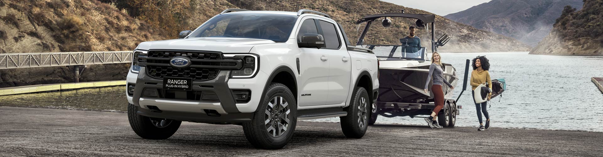 Three young adults stand by a ute on a boat ramp pulling a boat next to a lake