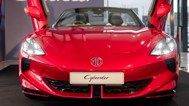 Front view of a red, 2024 MG Cyberster electric sports car with its doors open.
