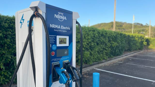 Blue EV charger in front of green hedge