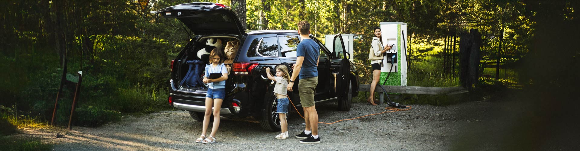 A family stands by their EV charging it in a bush setting
