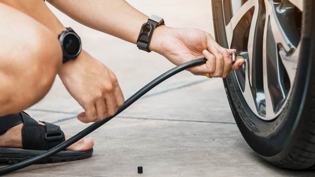 A man kneels to put air in the tyre of a car