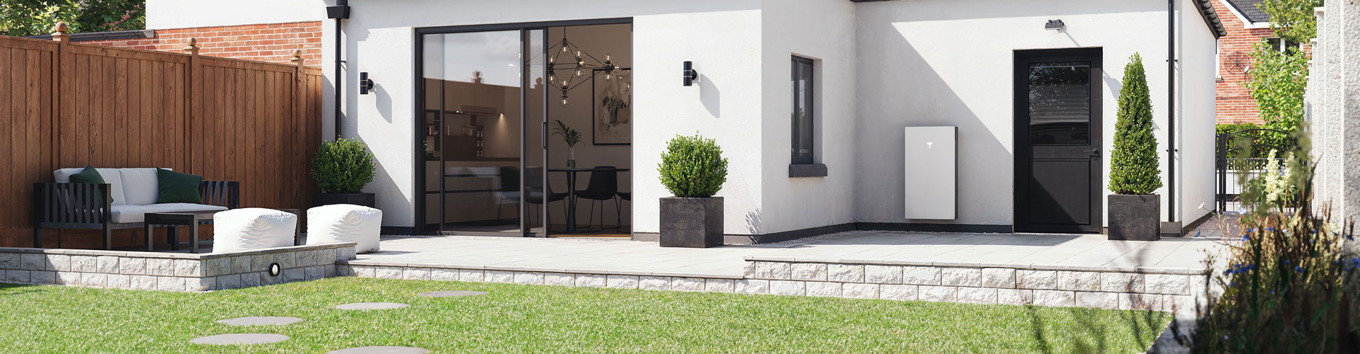 A Tesla powerwall battery on the back of a white house with part of garden visible