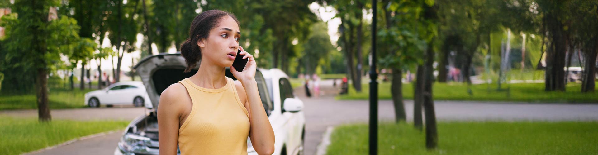 Young woman in orange singlet on phone in front of her white car