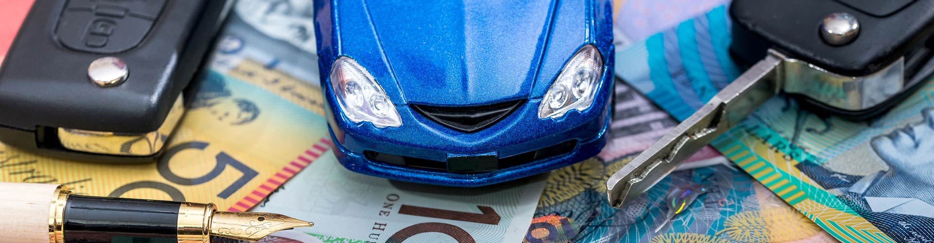 A blue toy car on some dollar bills next to car keys and a pen